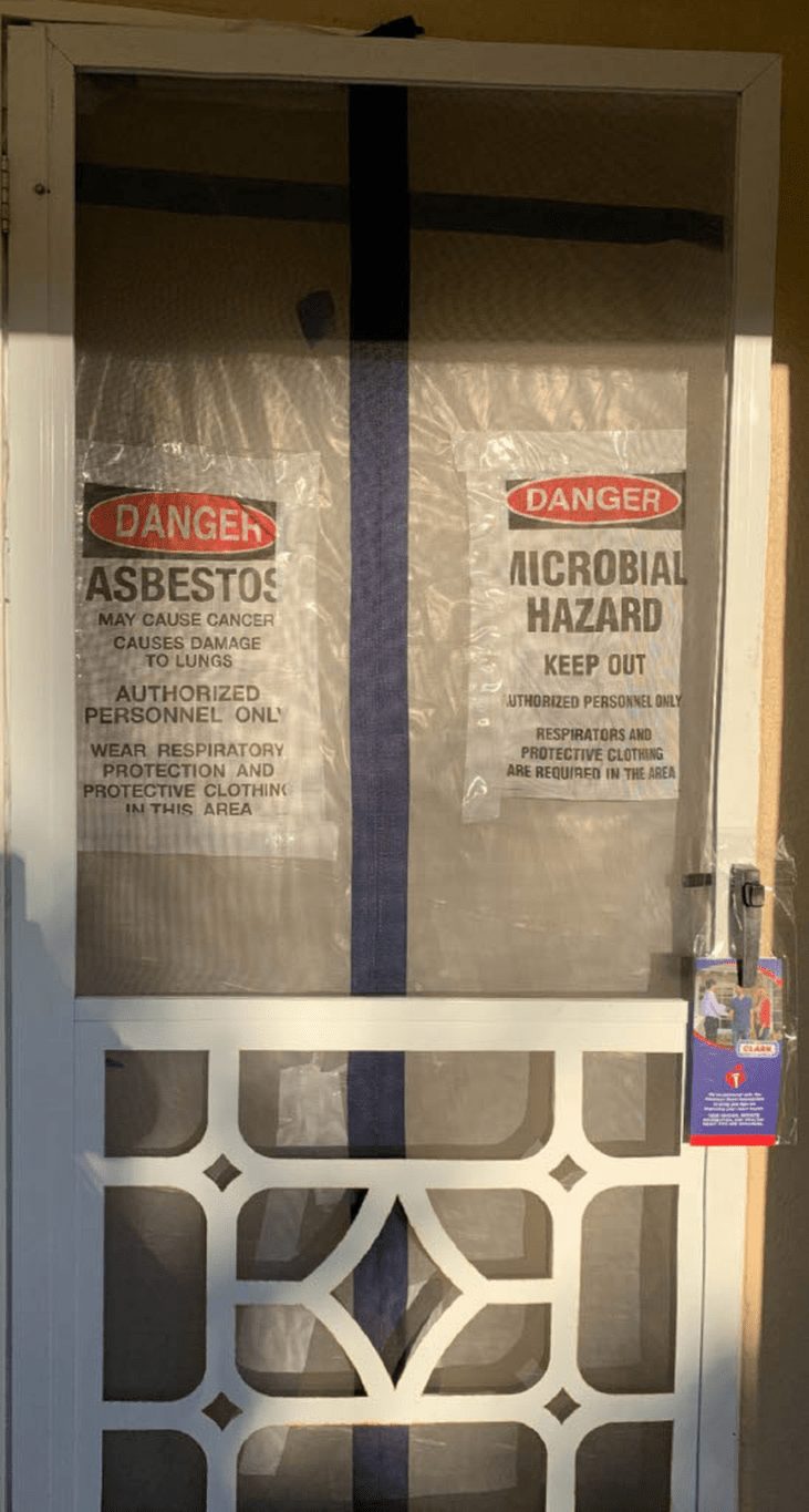Asbestos and microbial hazard warning placards taped to a sealed containment doorway at a Ventura County job site.