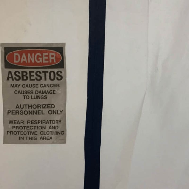 Danger asbestos warning placard posted on polyethylene containment sheeting at an active abatement work area.