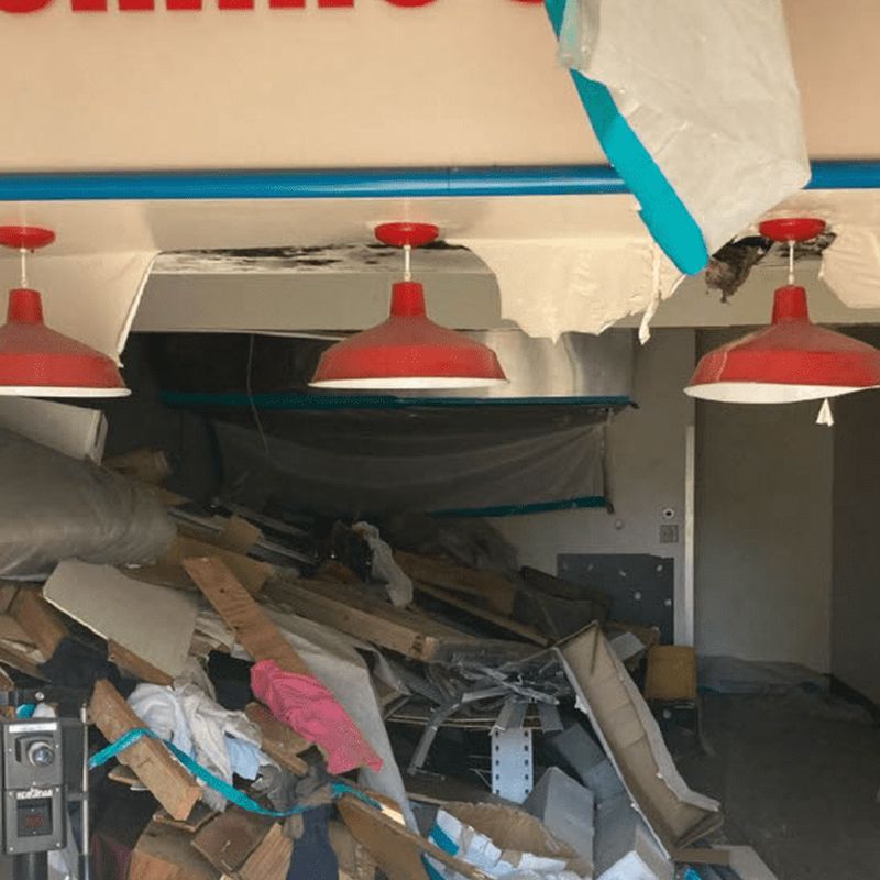 Commercial tenant space stripped to the shell with debris piled under containment sheeting during a pre-renovation survey.