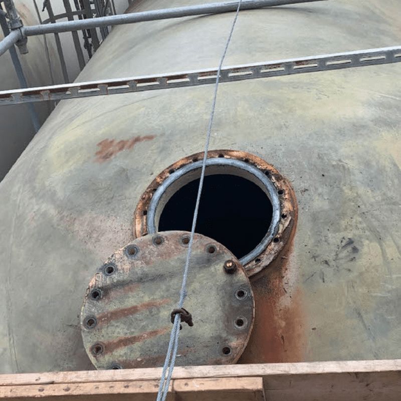 Open manway on a large industrial pressure vessel surrounded by scaffolding during an industrial inspection.